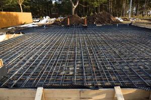 acessórios de ferro em uma área cega de madeira com tubos colocados são a base para despejar a fundação da casa com uma laje de concreto. construção de chalés, design, comunicações de engenharia. foto