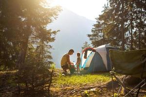 pai e filha de 2 anos perto de uma barraca em um acampamento na floresta nas montanhas. recreação ao ar livre em família, aventuras ecológicas, sobrevivência na natureza. foto