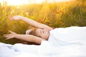 menina dorme na cama na grama, doce estica e boceja sonolenta, bom dia ao ar livre. ecologicamente correto, sono saudável, benefícios da ventilação, endurecimento, natureza limpa, ecologia, saúde infantil