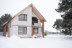 construção inacabada - uma casa feita de blocos porosos no inverno, suspensão durante a temporada de construção, congelada. neve e fachada da casa sem decoração exterior com janelas trapezoidais foto