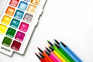 uma paleta de aquarelas coloridas com pincéis e marcadores em um fundo branco com espaço para texto. foto