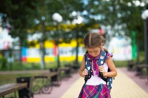 menina triste e chateada perto da escola com uma mochila. cansaço das aulas, ressentimento, lições não aprendidas, nota ruim. de volta à escola. espaço de cópia foto