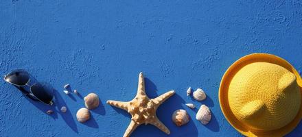 quadro com acessórios de praia em um chapéu de palha amarelo tema náutico, óculos de sol, estrela do mar e conchas em um fundo azul. conceito de férias, viagem marítima, proteção uv, natação. copie o espaço. flatlay foto