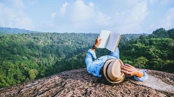 viagem de homem asiático relaxe no feriado. dormir relaxar ler livros em penhascos rochosos. no verão de montanha foto