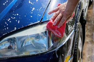 homem está lavando o carro lá fora. carro de limpeza manual. mão masculina segurando a esponja rosa com espuma. foto