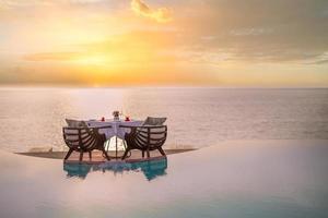 incrível jantar romântico na praia no deck de madeira com velas sob o céu pôr do sol. romance e amor, jantar de destino de luxo, configuração de mesa exótica com vista para o mar foto