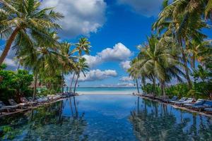 paisagem de turismo ao ar livre. luxuoso resort de praia com reflexo de piscina, cadeiras de praia ou espreguiçadeiras sob guarda-sóis com palmeiras e céu azul. conceito de plano de fundo de férias e viagens de verão foto