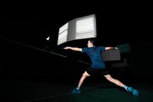 o jogador profissional de badminton usa a raquete com a peteca ou a peteca na quadra durante o aquecimento antes da competição do torneio em um único homem na quadra coberta foto