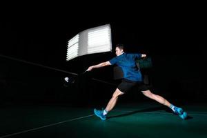 o jogador profissional de badminton usa a raquete com a peteca ou a peteca na quadra durante o aquecimento antes da competição do torneio em um único homem na quadra coberta foto