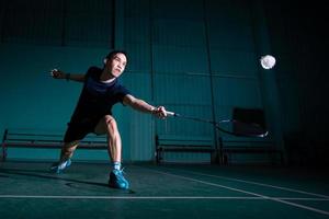 o jogador profissional de badminton usa a raquete com a peteca ou a peteca na quadra durante o aquecimento antes da competição do torneio em um único homem na quadra coberta foto