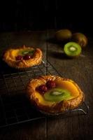 torta de frutas com kiwi, cereja, caqui, coloque em tira de aço no banco de madeira com fundo preto foto