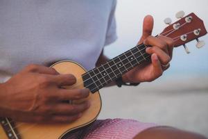 feche um homem tocando violão ukulele na praia com efeito de luz. foto