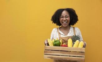 feliz entrega da mulher afro-americana carregando carrinho cheio de produtos orgânicos tropicais da horta local para ingrediente vegano e vegetariano foto