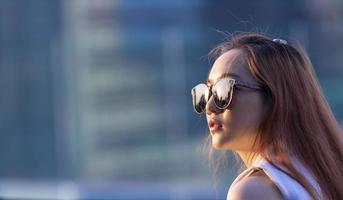 modelo de mulher asiática com cabelo ruivo usando óculos escuros enquanto olha diretamente para o sol com espaço de cópia foto