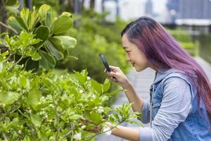 estudante asiático usando lupa para explorar o inseto no jardim para aula de biologia depois da escola no parque para o conceito de educação natural e ambiental foto