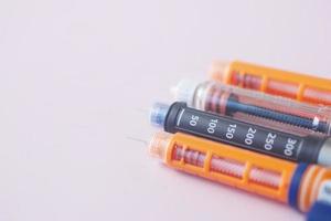 muitas canetas de insulina em fundo rosa claro foto