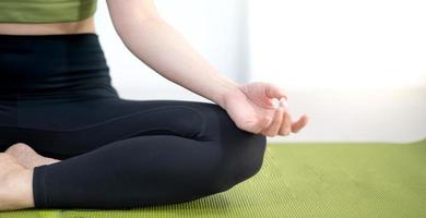 mulher praticando aula de ioga, respirando, meditando sentado em um tapete de ioga verde, em casa. foto