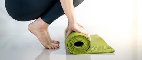 mão feminina rolando tapete de ioga verde para preparar o exercício no tapete. foto