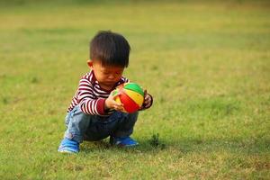 menino asiático jogando futebol no parque. criança com brinquedo de bola no campo de grama. foto