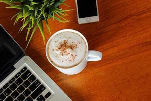 laptop, telefone inteligente e uma xícara de café com leite quente na mesa de madeira vista superior atirou. foto