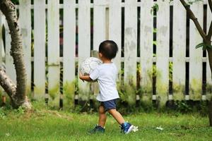 menino asiático jogando futebol no parque. garoto com bola no campo de grama. foto