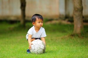 menino asiático jogando futebol no parque. garoto com bola no campo de grama. foto