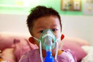 menino asiático fazendo inalação com um nebulizador no hospital. Criança doente. foto