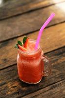 copo de smoothie de morango e morangos frescos por cima e tem fundo de madeira. conceito de comida e bebida saudável. foto