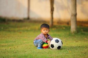 menino asiático jogando futebol no parque. criança com brinquedo de bola no campo de grama. foto