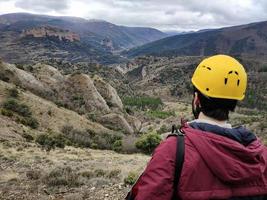 jovem com capacete de escalada amarelo olhando a paisagem montanhosa foto