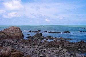 praia de pedra com vista para o mar azul e céu azul nublado brilhante foto