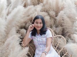 sorria mulher asiática em vestido casual sente-se no jardim de flores de grama macia e seca foto