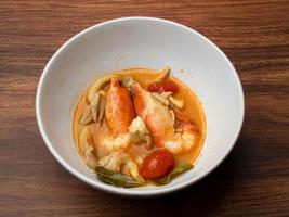 sopa de camarão quente e picante ou comida tailandesa tom yum goong em tigela branca na mesa de madeira foto