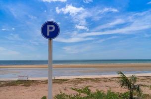 p assinar no símbolo de tráfego de círculo para estacionar perto da vista da praia com céu azul nublado brilhante. dia ensolarado. verão foto