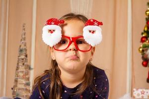 menina usando óculos de papai noel e fazendo caretas foto