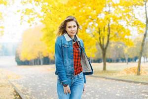 menina bonita com roupas jeans e uma camisa xadrez vermelha no parque outono. foto