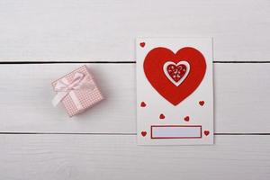 um presente e um cartão com corações vermelhos em cima da mesa. foto
