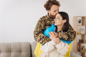 casal ucraniano, militar de uniforme abraça e envolve sua esposa na bandeira ucraniana. o conceito de patriotismo. foto