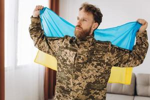 retrato de um jovem soldado patriota ucraniano barbudo emocional em uniforme militar segurando uma bandeira no escritório foto