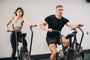 jovem e mulher usando bicicleta de ar para treino cardio no ginásio de treinamento cruzado foto