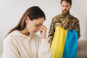uma mulher ucraniana lamenta e se despede de seu marido militar em um uniforme segurando uma bandeira ucraniana em casa foto