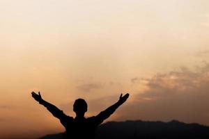 silhueta de um homem levanta as mãos e oração ao pôr do sol. conceito de religião. foto