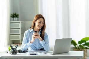 jovem mulher bonita usando seu laptop enquanto está sentado em uma cadeira em seu local de trabalho. foto