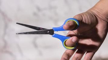 feche a mão masculina segurando uma tesoura azul e amarela sobre fundo branco abstrato foto