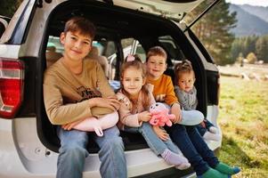 família de quatro filhos no interior do veículo. crianças sentadas no porta-malas. viajando de carro nas montanhas, conceito de atmosfera. foto