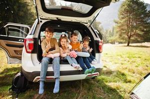 família de quatro filhos no interior do veículo. crianças sentadas no porta-malas. viajando de carro nas montanhas, conceito de atmosfera. foto