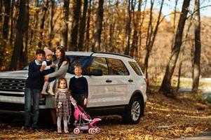 mãe fica perto de carro suv branco com quatro filhos no parque outono. caminhada em família na floresta de outono. foto