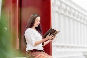 mulher budista asiática usando vestido tradicional da tailândia lendo livro de dharma foto