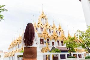 jovem mulher asiática vestindo vestido tradicional da tailândia rezando em wat ratchanatdaram uma famosa atração turística e locais de interesse em bangkok tailândia foto