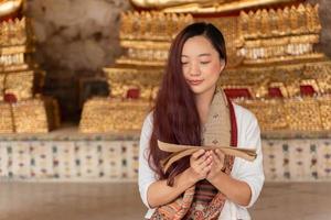 retrato jovem mulher asiática vestindo vestido tradicional da tailândia lendo sânscrito antigo livro tripitaka do senhor buda dhamma foto